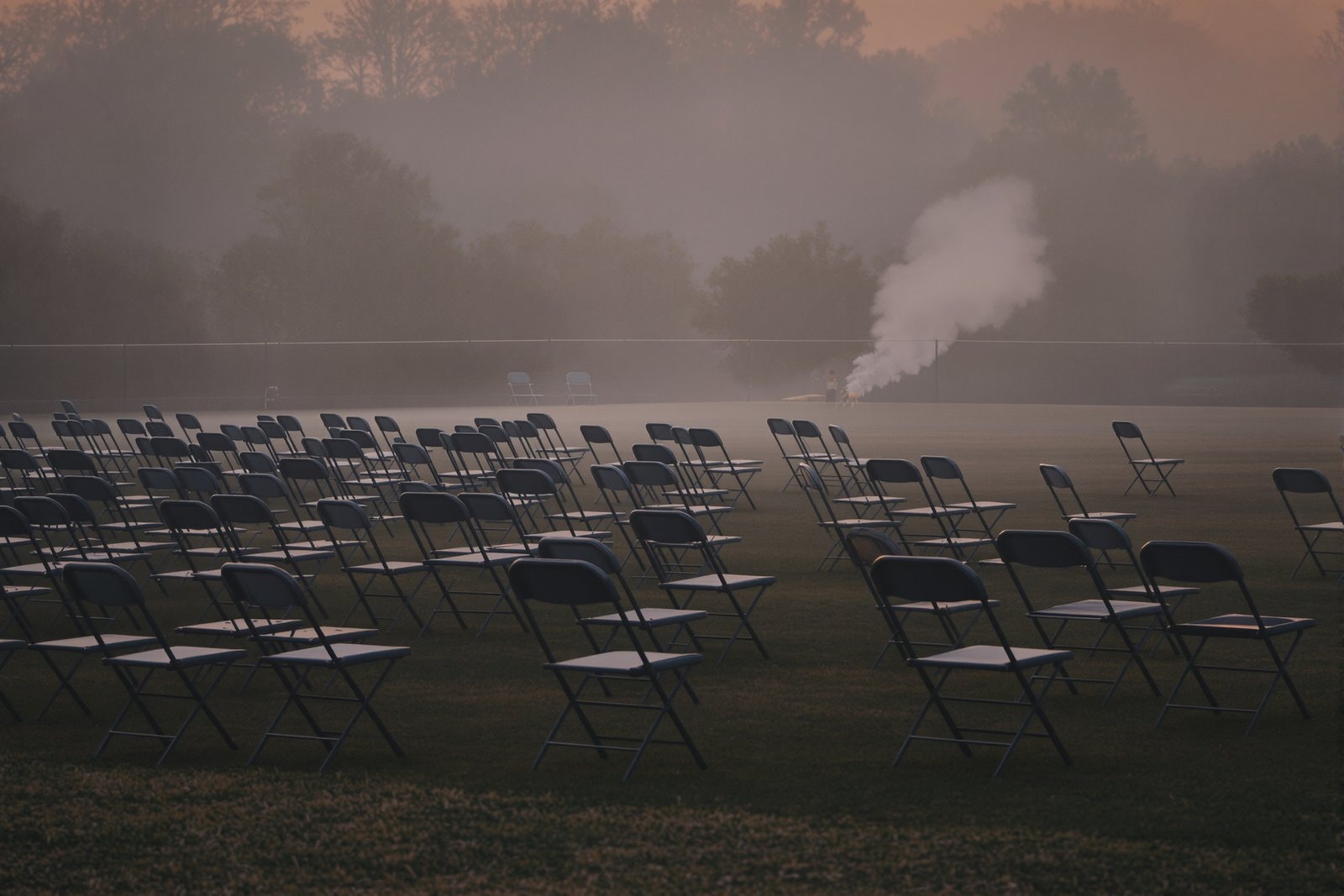 Rows of empty folding chairs on a misty grass field at dawn