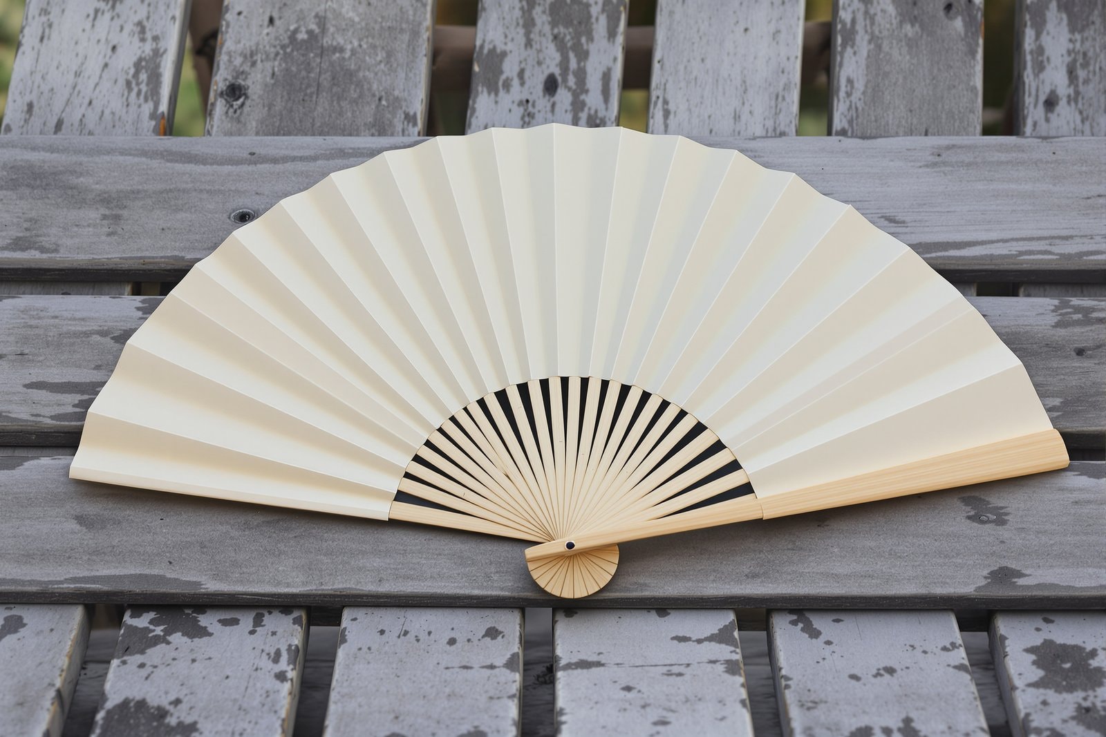 A closed and partly opened plain cream paper fan with bamboo ribs on a weathered wooden bench