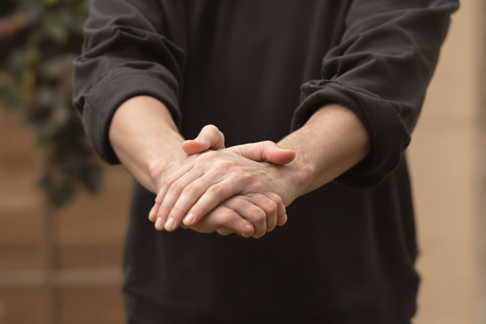 Two hands resting lightly one over the other in front of a dark cotton shirt, face not shown