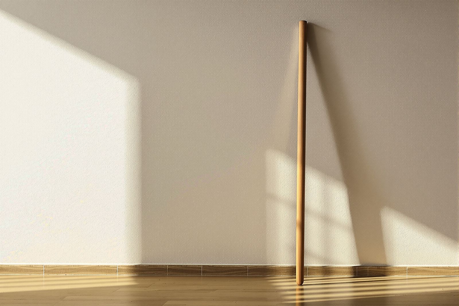 A plain wooden staff leaning against a warm plaster wall in afternoon light
